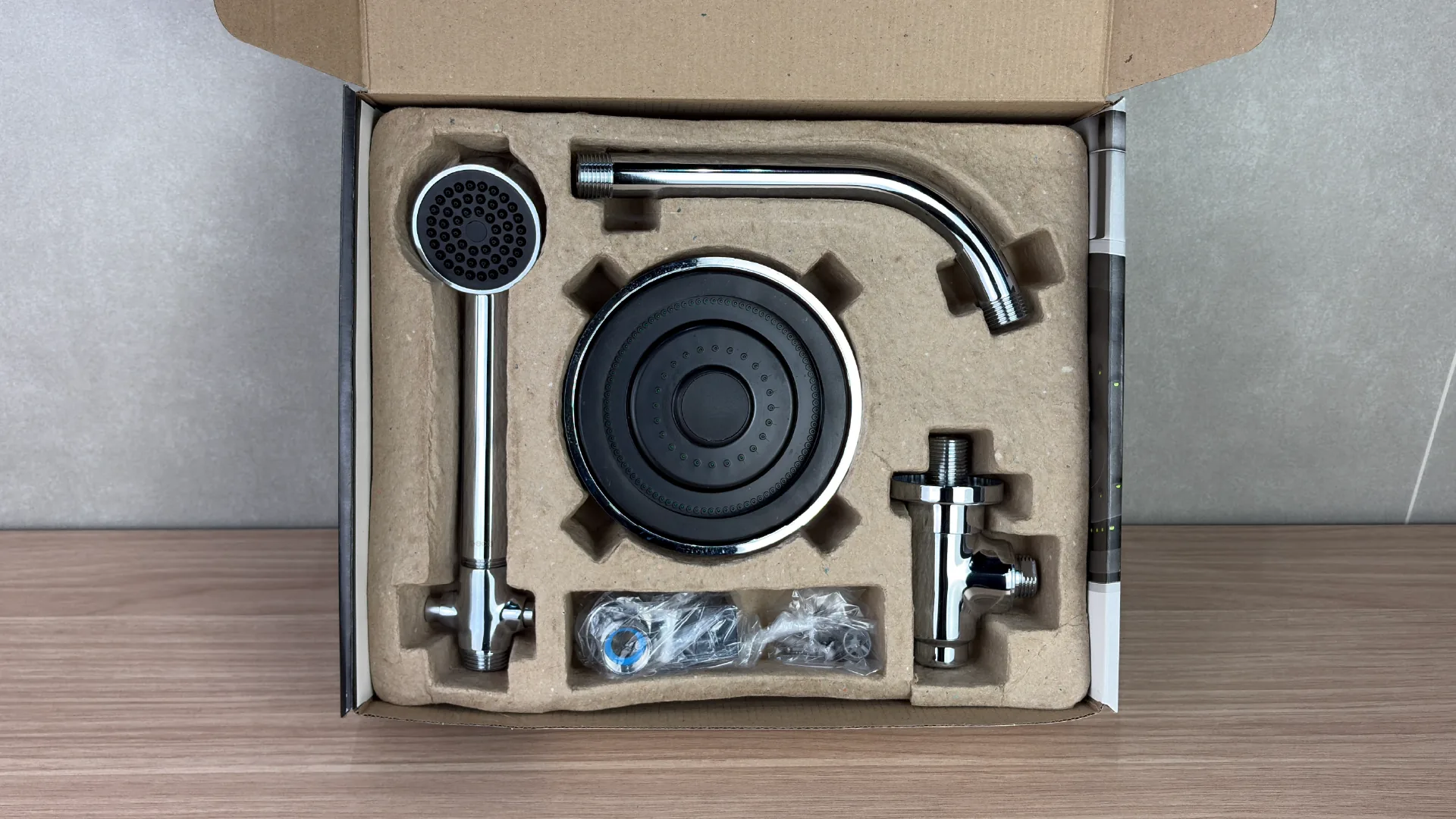 The pack opened seen from above: the moulded pulp tray locking the showerhead, the hand shower, the wall arm, the diverter and the accessories bag, each in its own recess.