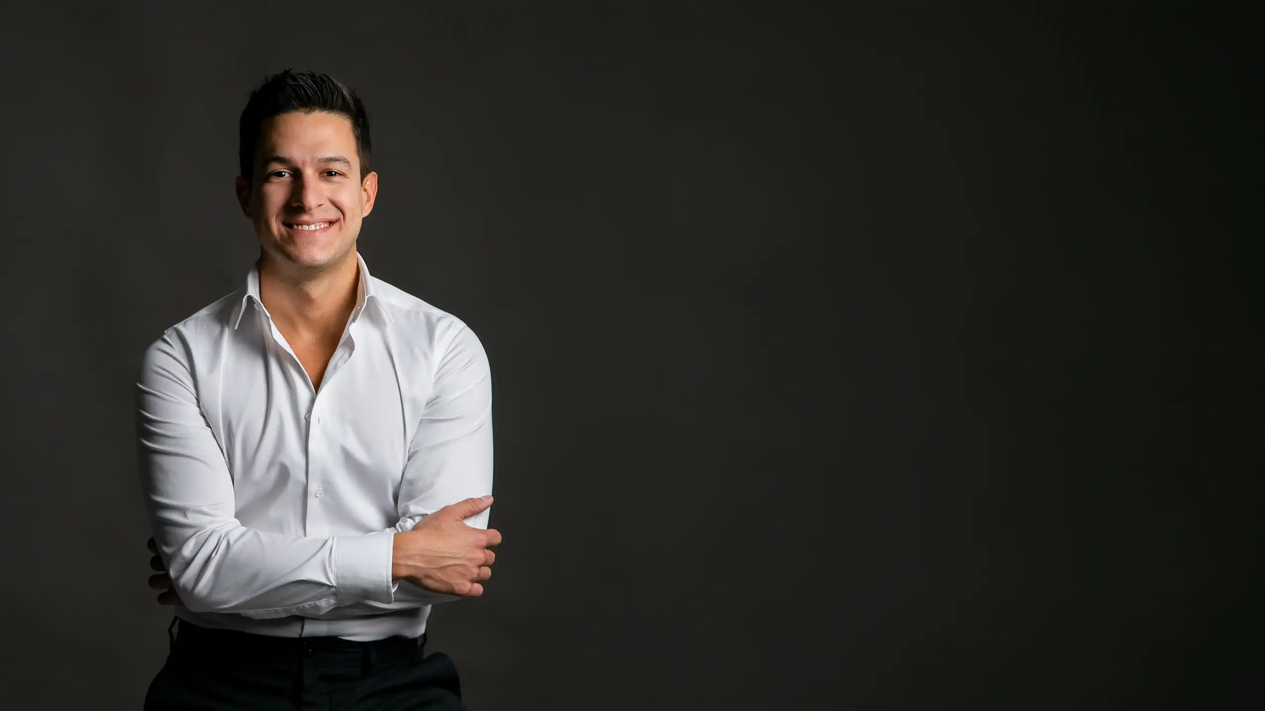 Hugo Zuffo, Senior Packaging Designer, mit verschränkten Armen im weißen Hemd vor dunklem Hintergrund.
