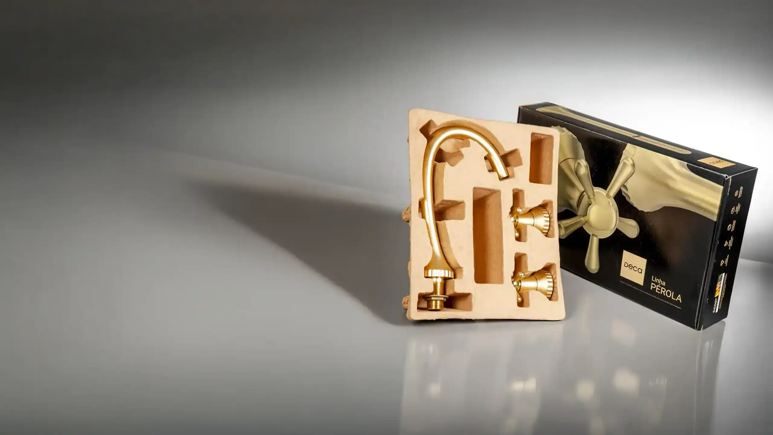 Moulded pulp tray holding the gold Pérola tap, next to the closed box in black and gold.