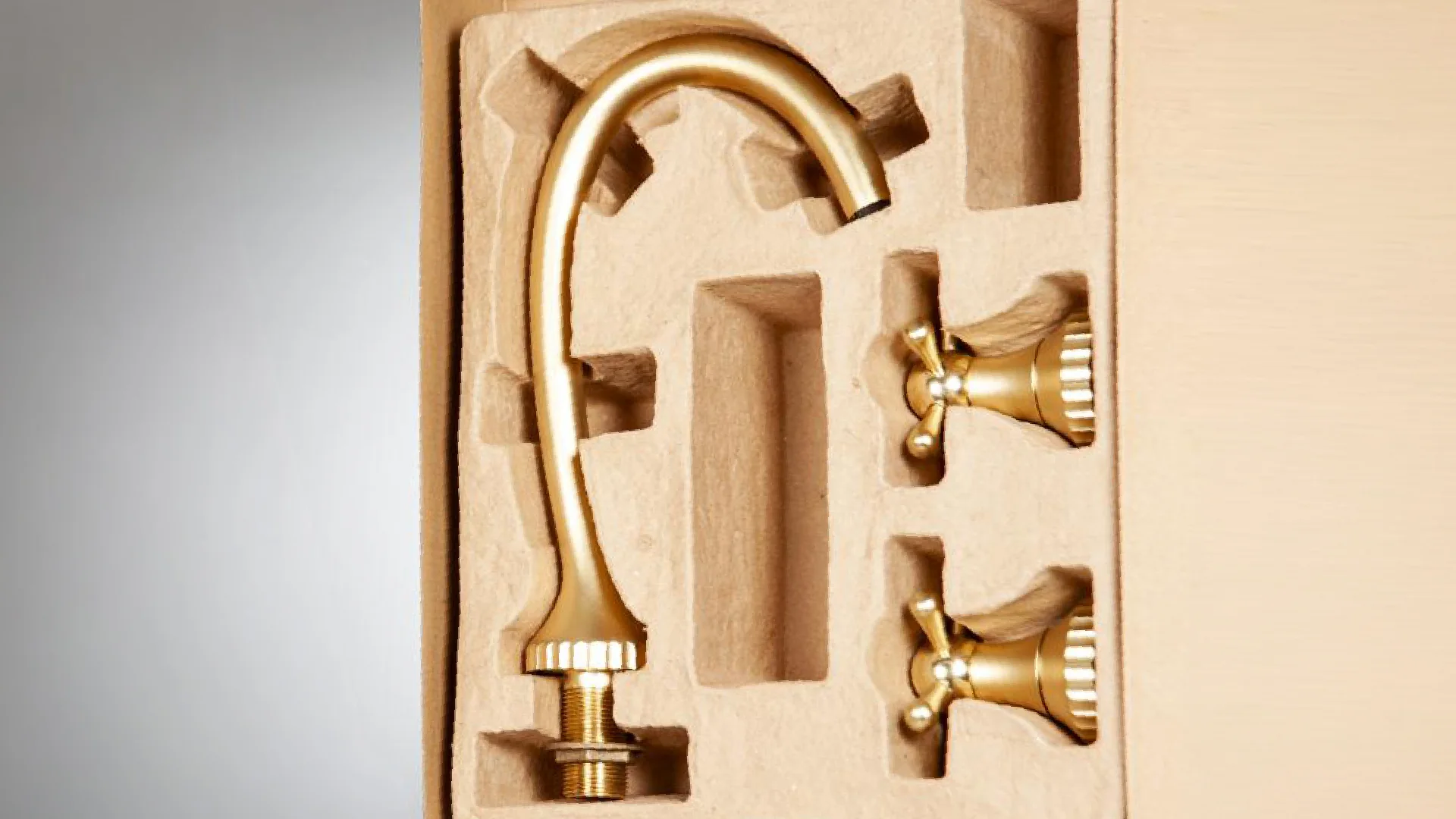 Close-up of the moulded pulp tray with the curved spout and the tap's two handles seated in their recesses.