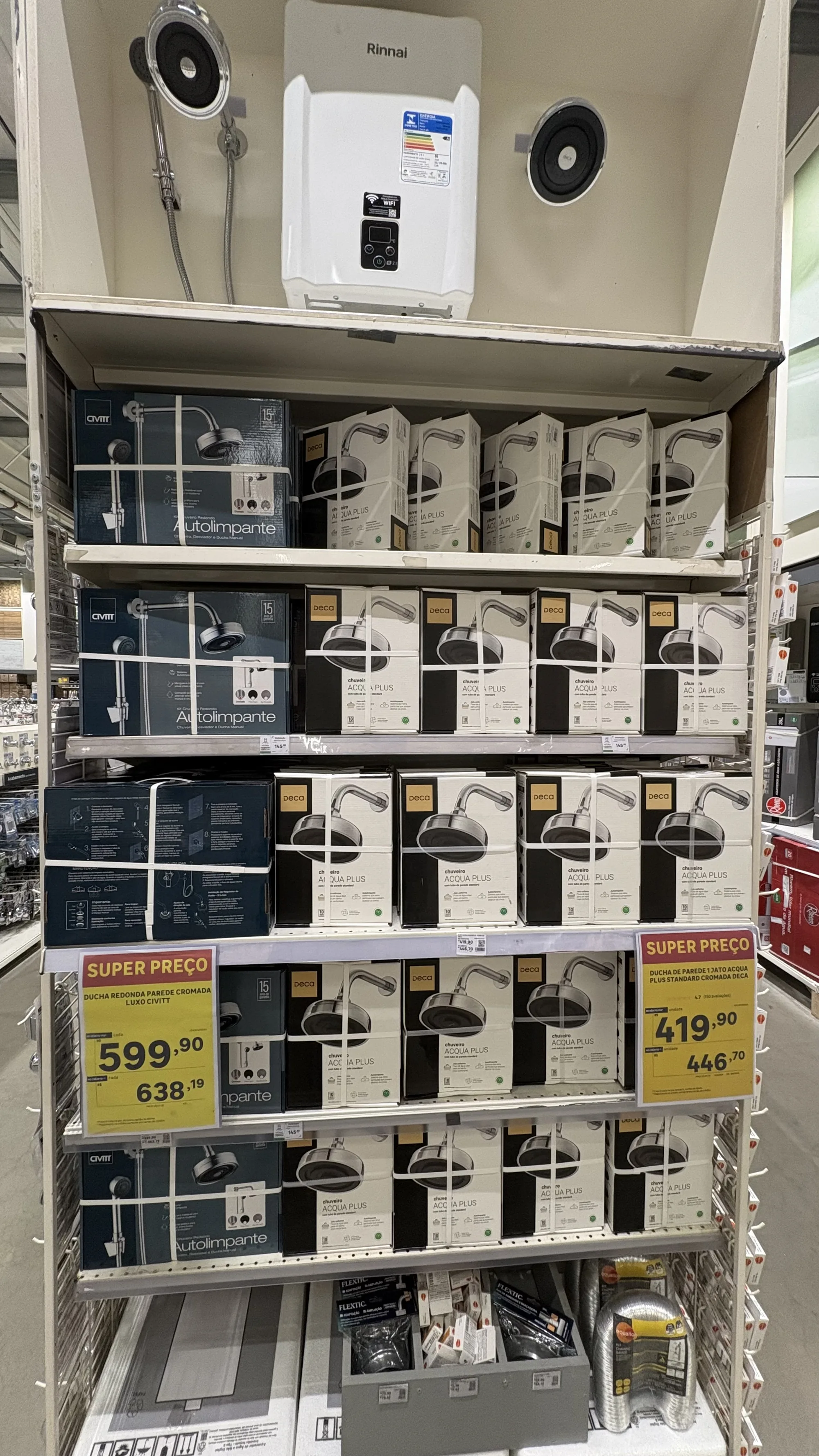 Gôndola de chuveiros vista de frente, com cinco prateleiras de caixas do Deca Acqua Plus repetidas, etiquetas de super preço e um aquecedor Rinnai acima.