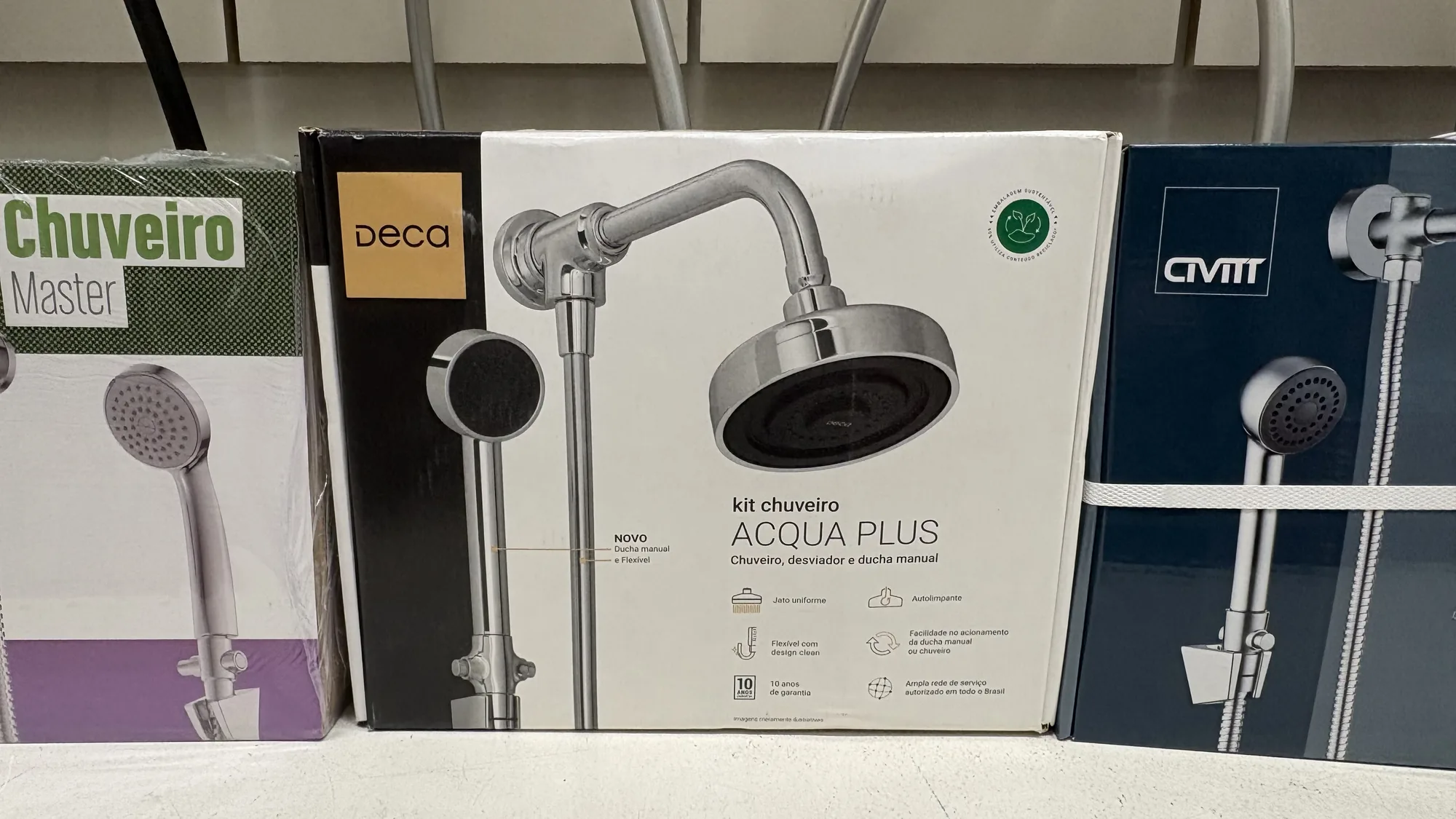 Caixa do kit de chuveiro Deca Acqua Plus na prateleira, entre uma embalagem da Chuveiro Master e uma da Civitt.