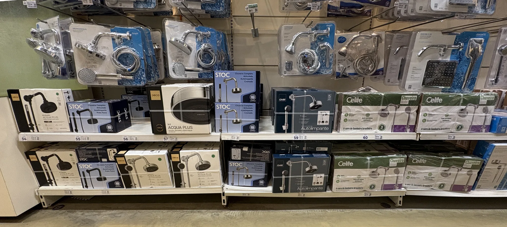Prateleira longa de um home center com caixas de chuveiro e acessórios de várias marcas, entre elas o Deca Acqua Plus, e blisters pendurados acima.