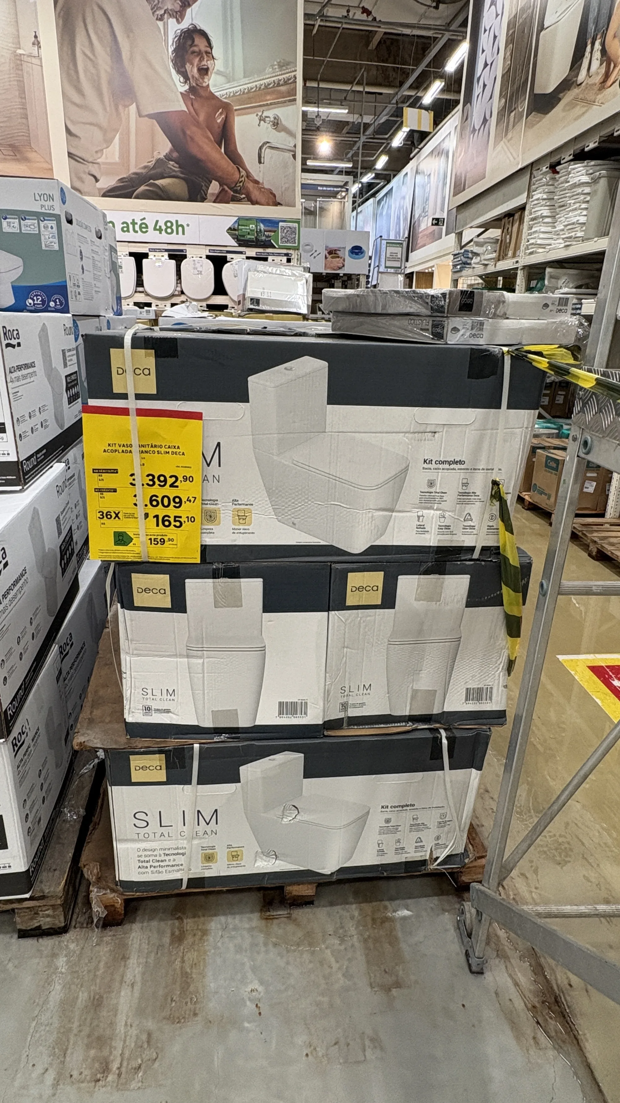 Pallet com três camadas de caixas do vaso sanitário Deca Slim Total Clean, com etiqueta amarela de preço parcelado e caixas da Roca e da Lyon ao lado.