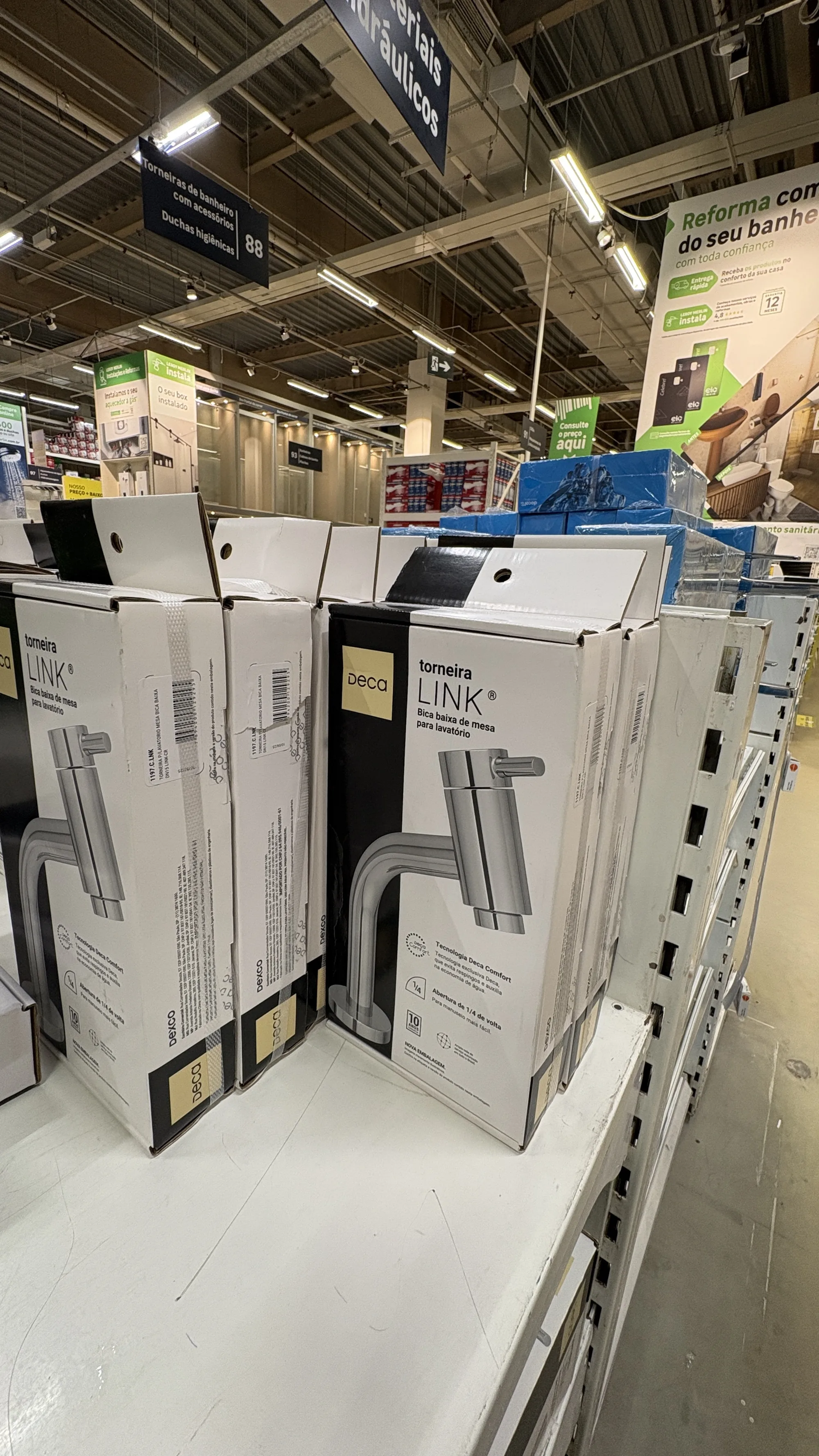 Prateleira de torneiras de um home center com várias caixas da linha Deca Link, sob a placa do corredor 88 de materiais hidráulicos.