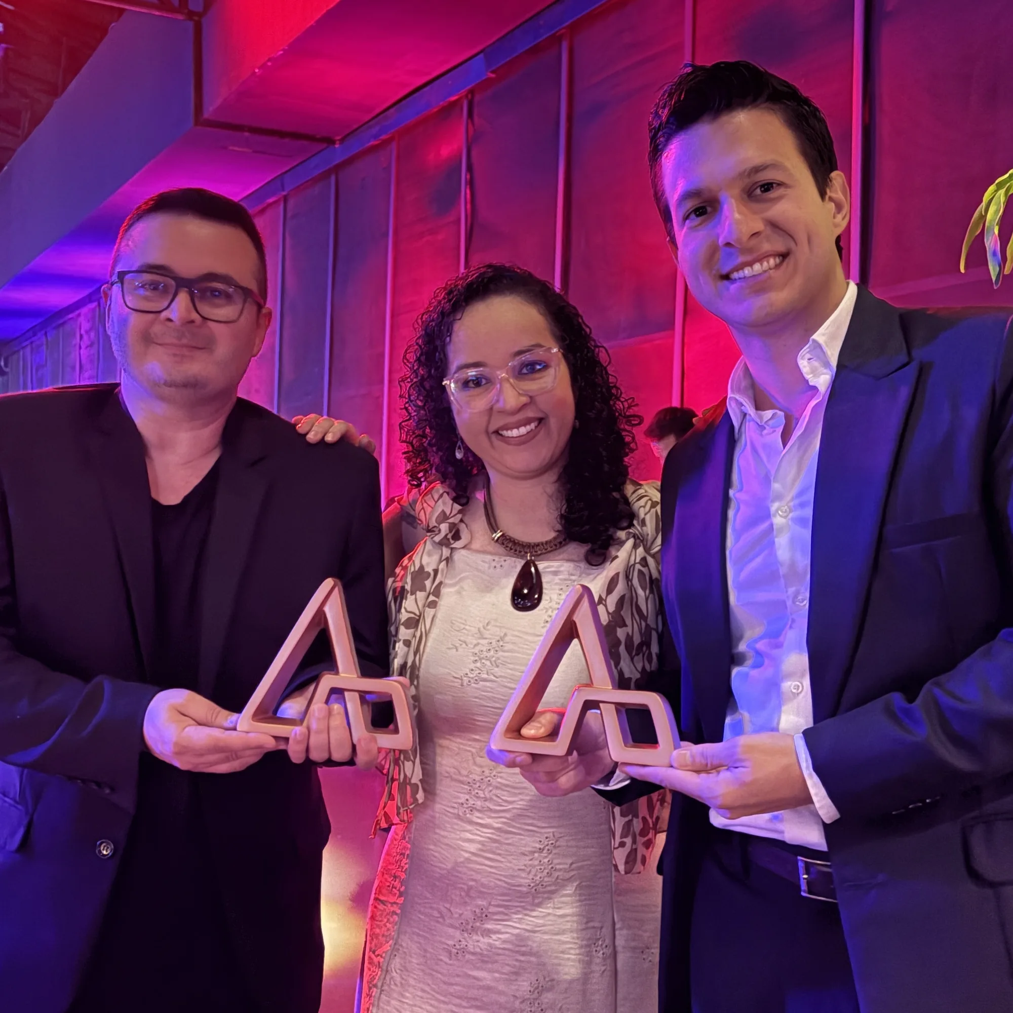 Hugo Zuffo, on the right, holding the triangular trophy of the Prêmio ABRE da Embalagem Brasileira 2026, next to two people also holding their trophies, at the ceremony in São Paulo.