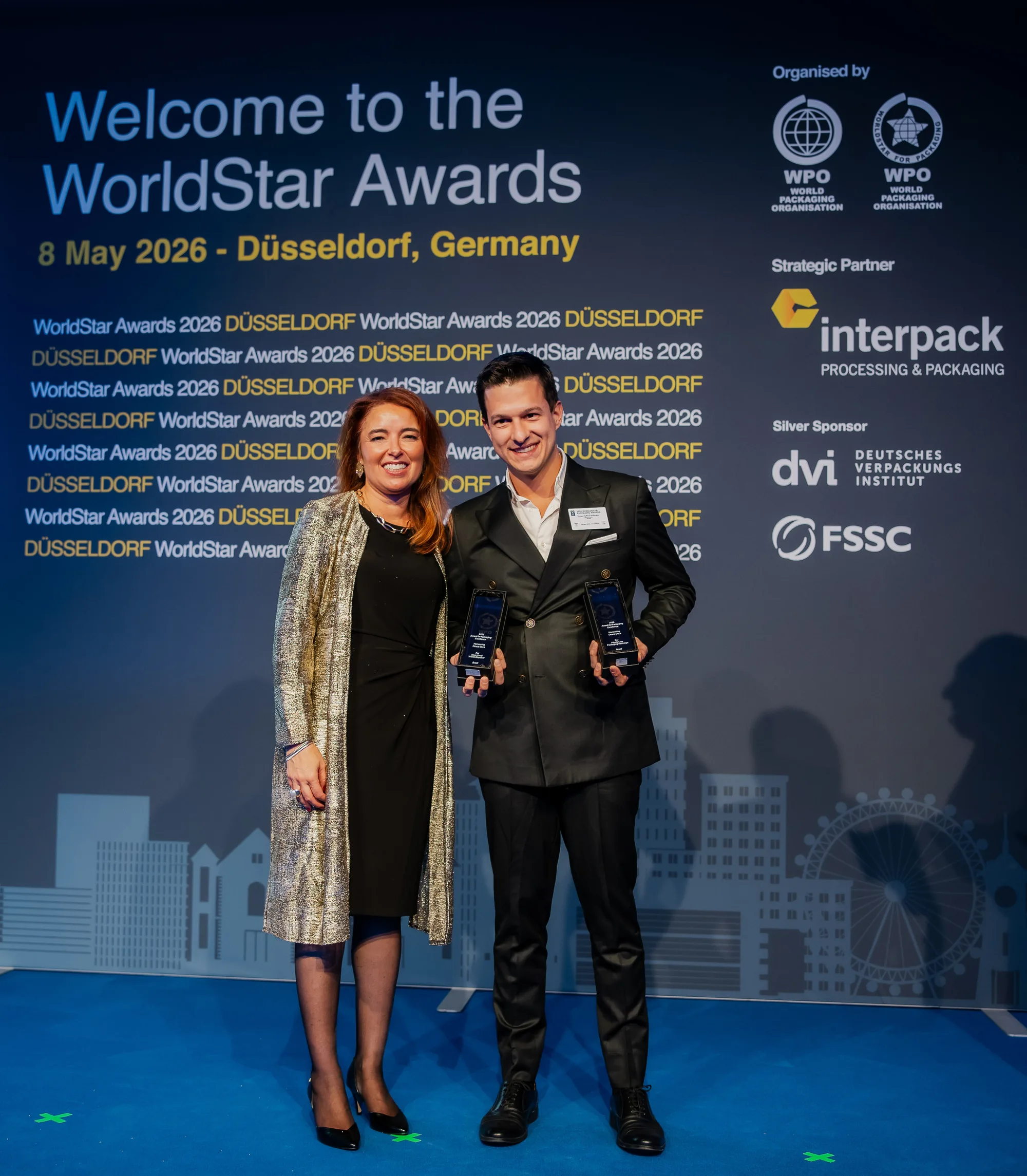 Hugo Zuffo holding the two WorldStar Packaging Awards 2026 trophies, next to a World Packaging Organisation representative, in front of the event backdrop in Düsseldorf.